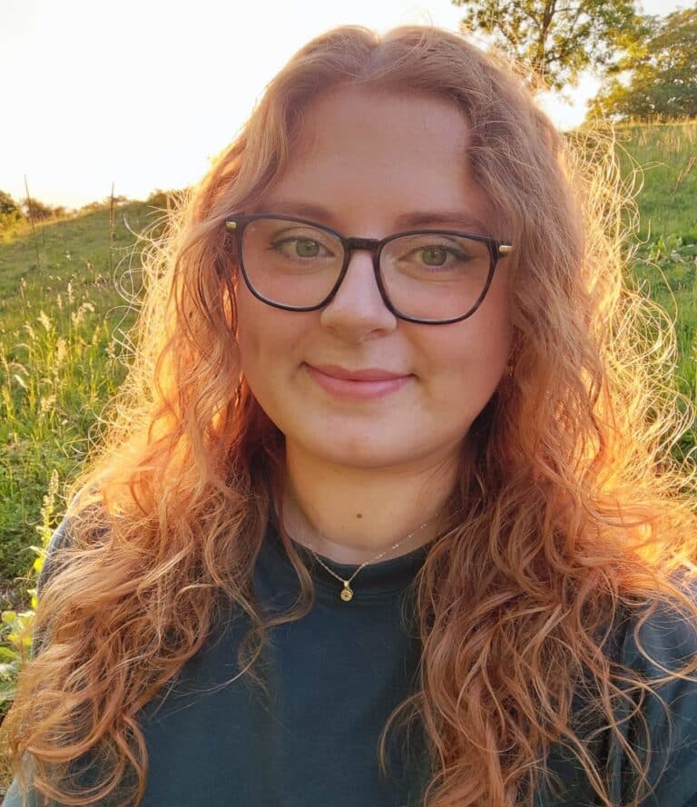 Porträtfoto einer rothaarigen Frau mit Brille im Freien, fotografiert bei warmem Sonnenlicht.